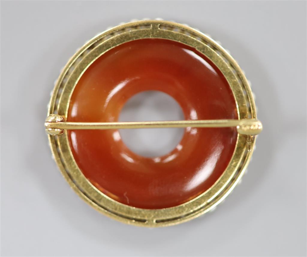 An early 20th century yellow metal(stamped 14), carved carnelian and seed pearl set openwork circular brooch, 27mm, gross 6.4 grams.